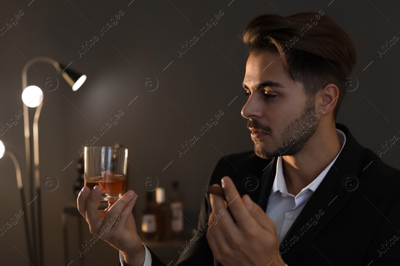 Photo of Young man with glass of whiskey and cigar at home