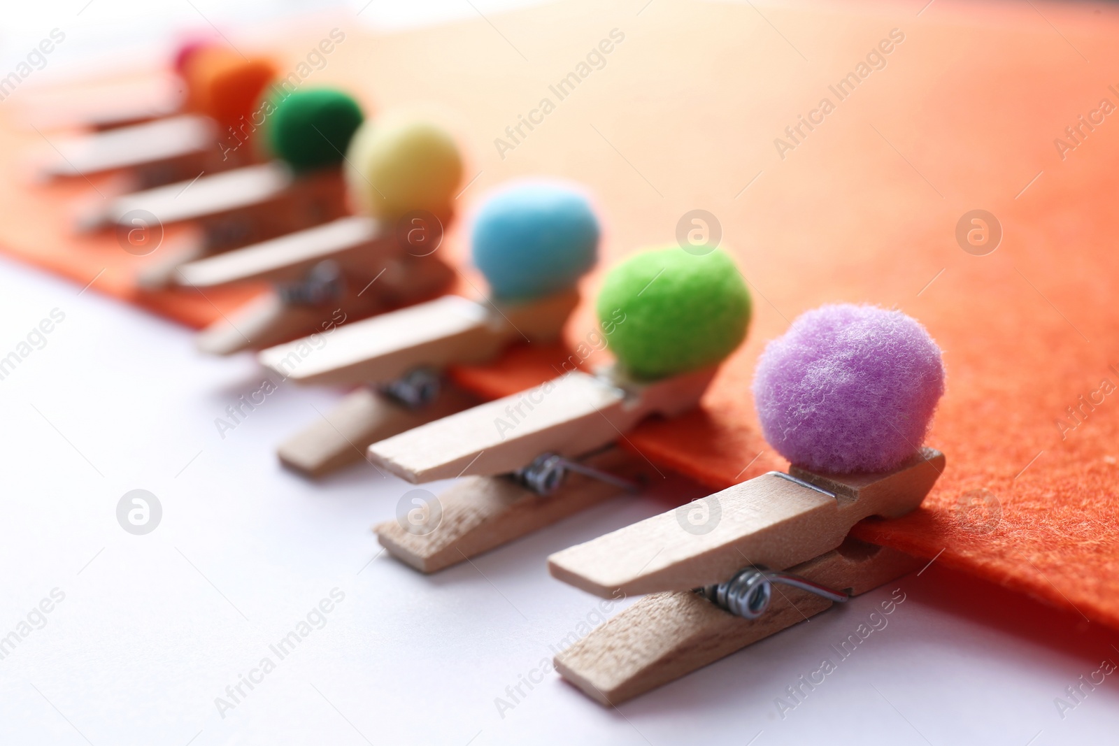 Photo of Sheet of orange felt with clothespins and small soft balls on white background, closeup