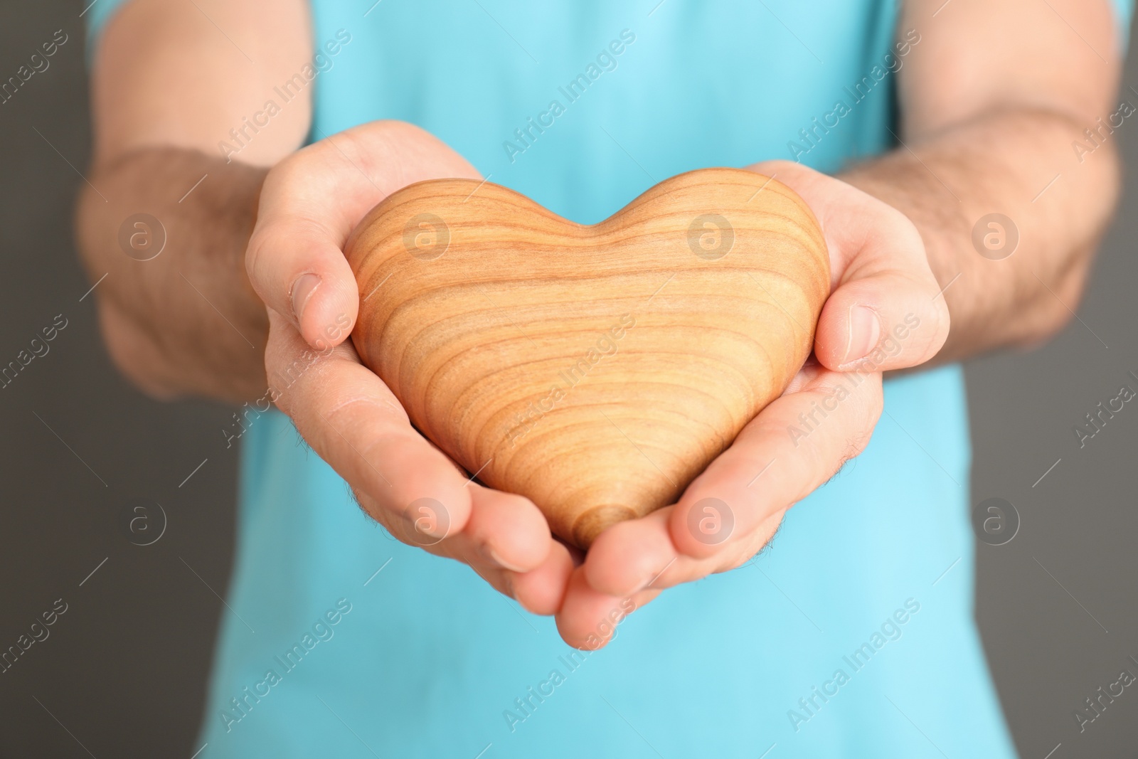 Photo of Young man holding wooden heart in his hands on grey background, closeup