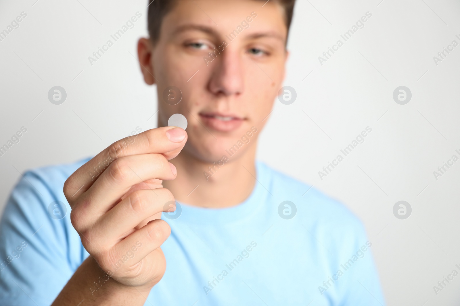 Photo of Teen guy using acne healing patch against light background, focus on hand