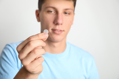 Teen guy using acne healing patch against light background, focus on hand