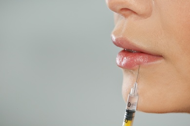 Young woman getting lips injection on grey background, space for text. Cosmetic surgery