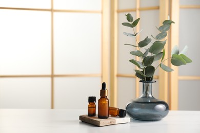 Aromatherapy. Bottles of essential oil and eucalyptus leaves on white table, space for text