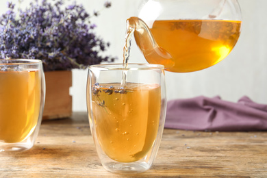 Pouring delicious lavender tea into glass on wooden table