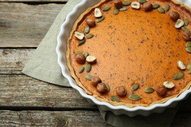 Photo of Delicious pumpkin pie with seeds and hazelnuts on wooden table. Space for text