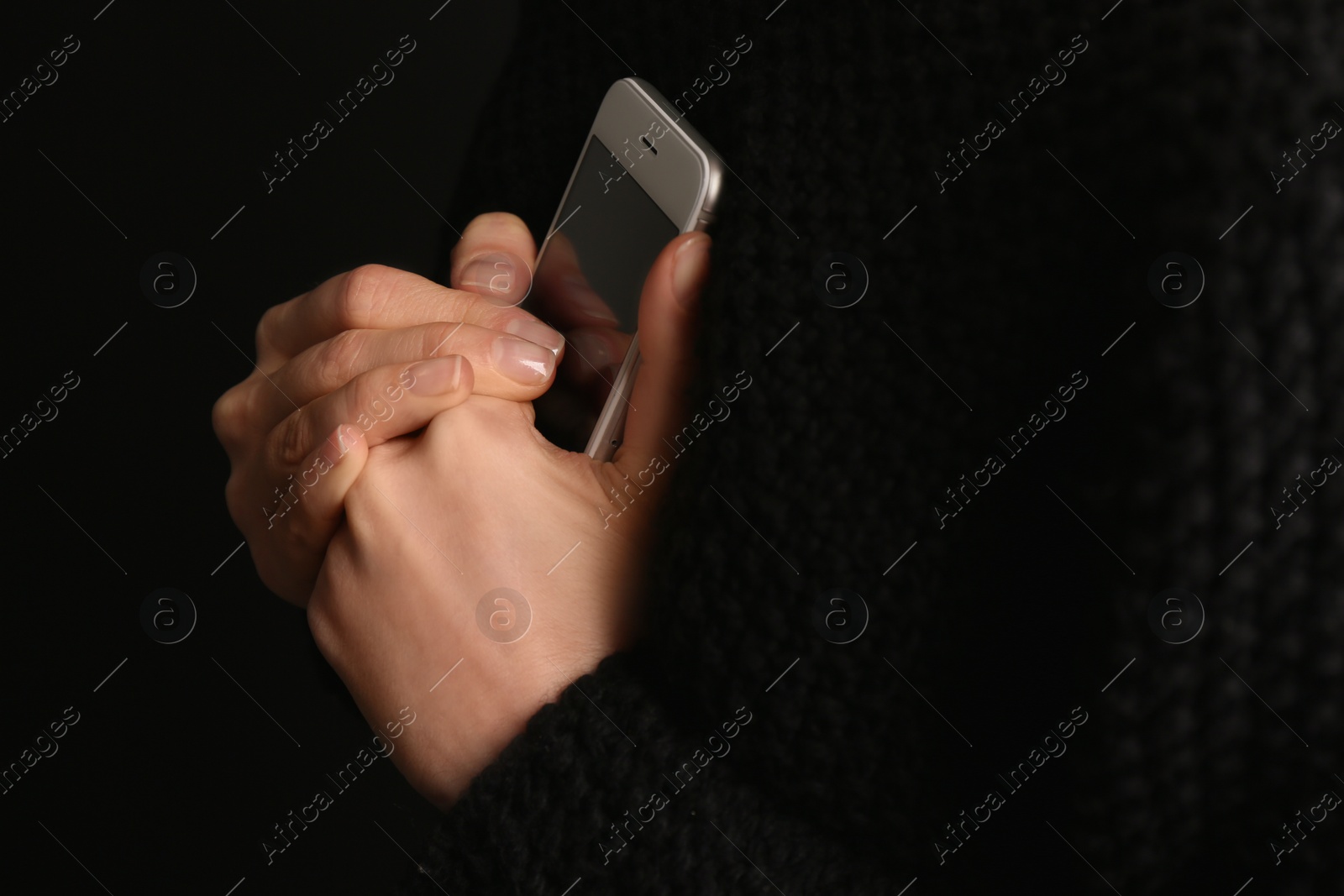 Photo of Lonely woman holding smartphone on black background, closeup. Space for text