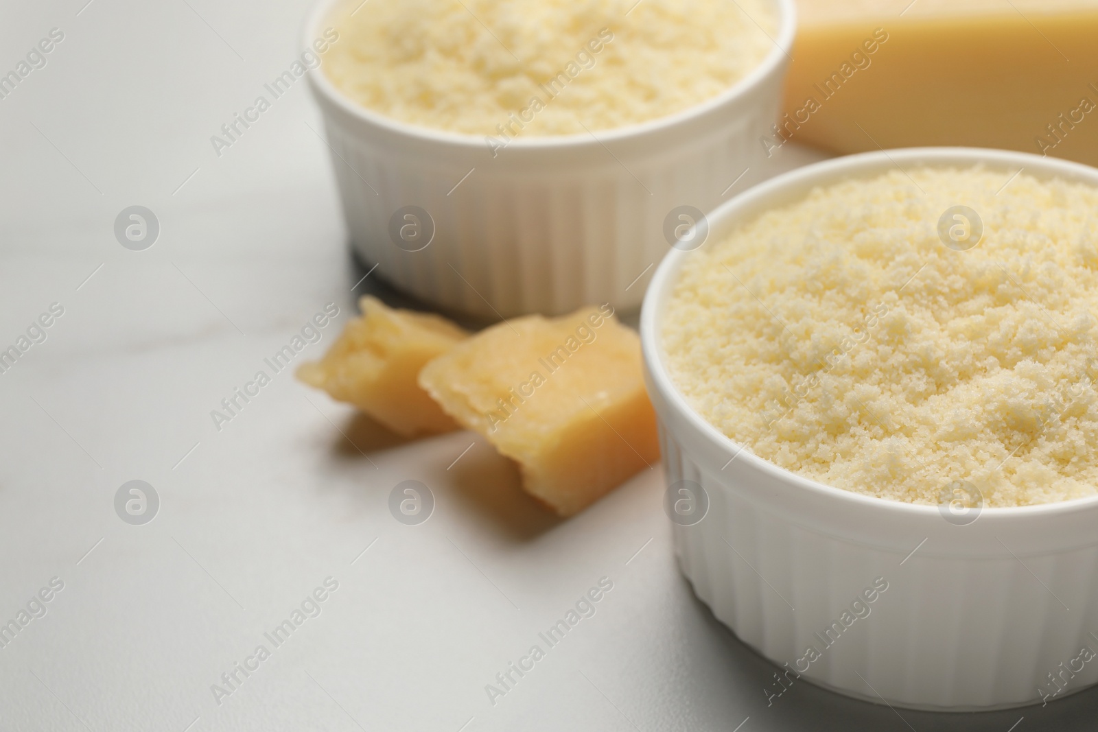 Photo of Bowl with grated parmesan cheese on white marble table, closeup. Space for text