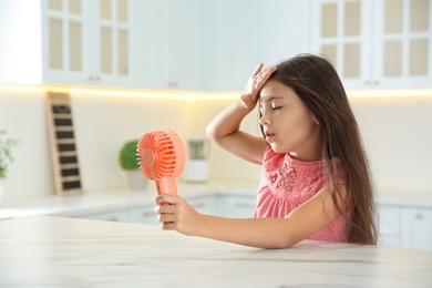 Little girl with portable fan suffering from heat at home. Summer season