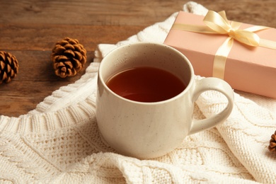 Photo of Composition with cup of hot winter drink and warm knitted sweater on wooden background. Cozy season