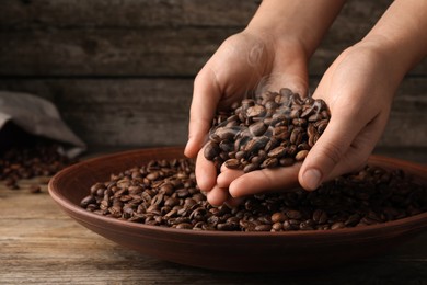 Image of Woman taking pile of aromatic roasted coffee beans from bowl at wooden table, closeup