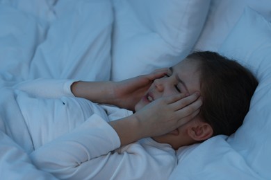 Photo of Little girl suffering from headache in bed at night