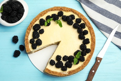 Photo of Delicious cheesecake decorated with blackberries on blue wooden table, flat lay