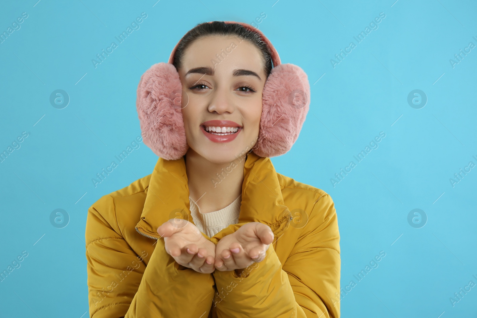 Photo of Beautiful young woman wearing earmuffs on light blue background