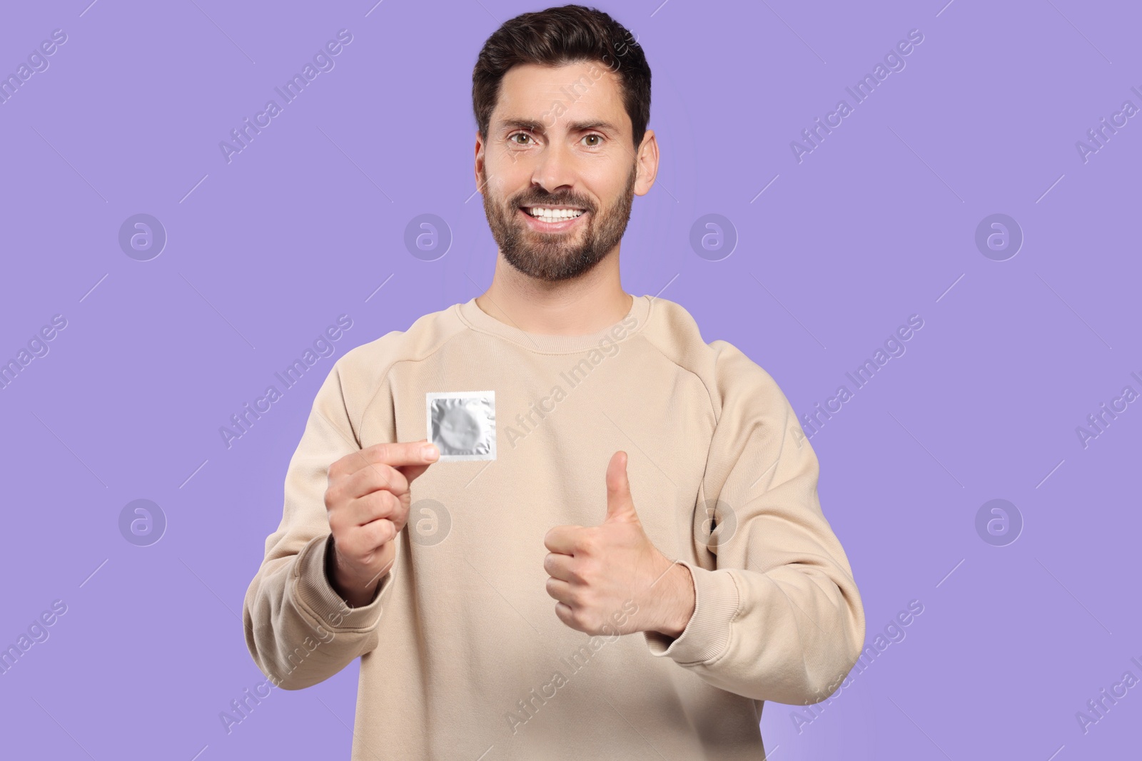 Photo of Happy man with condom showing thumb up on purple background. Safe sex