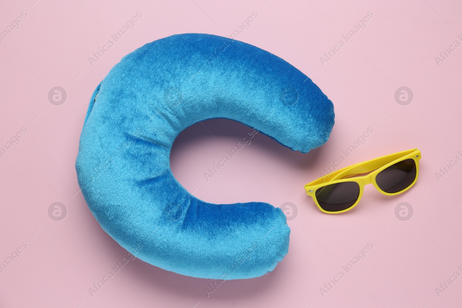 Photo of Light blue travel pillow and sunglasses on pink background, flat lay