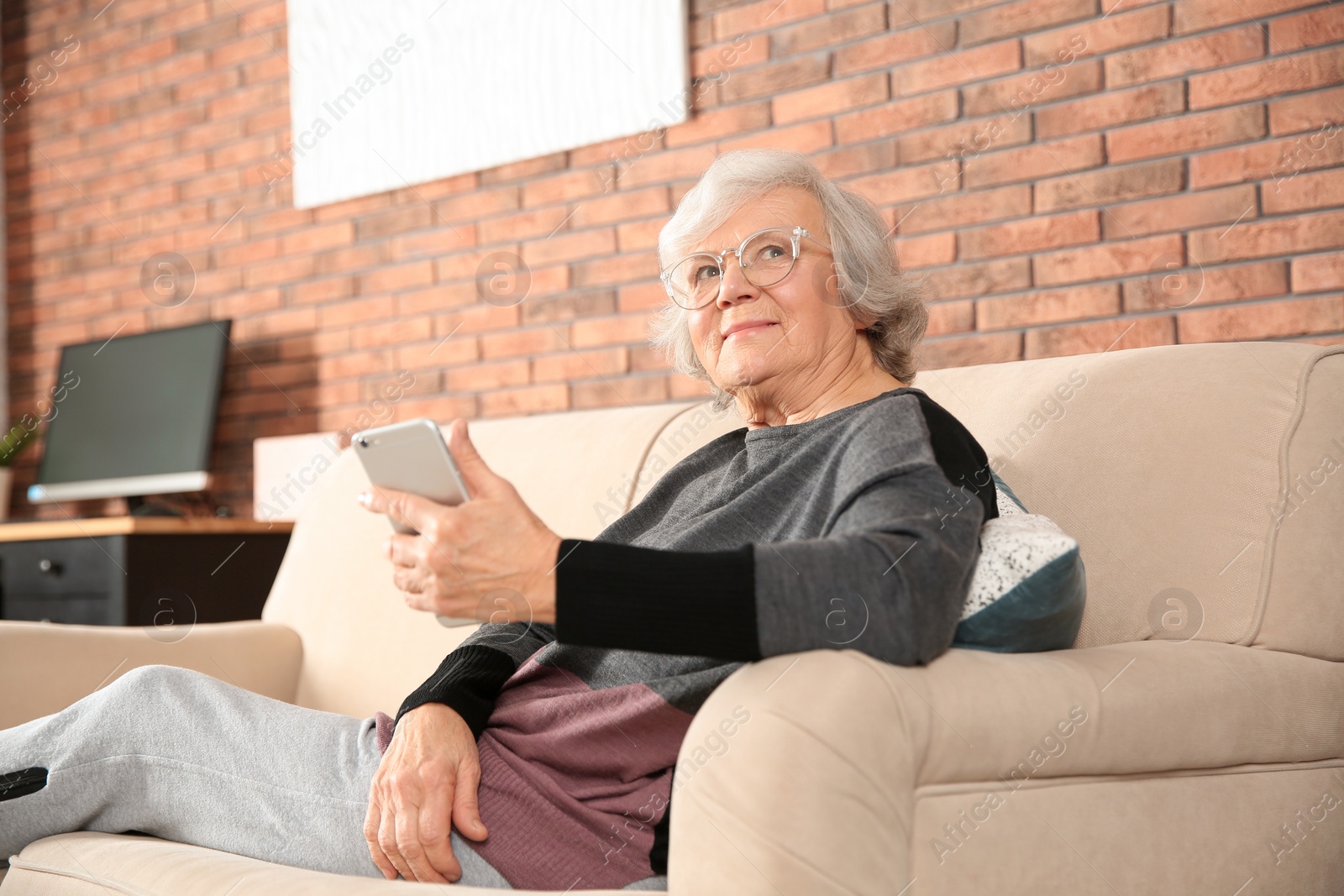 Photo of Elderly woman using smartphone on sofa in living room