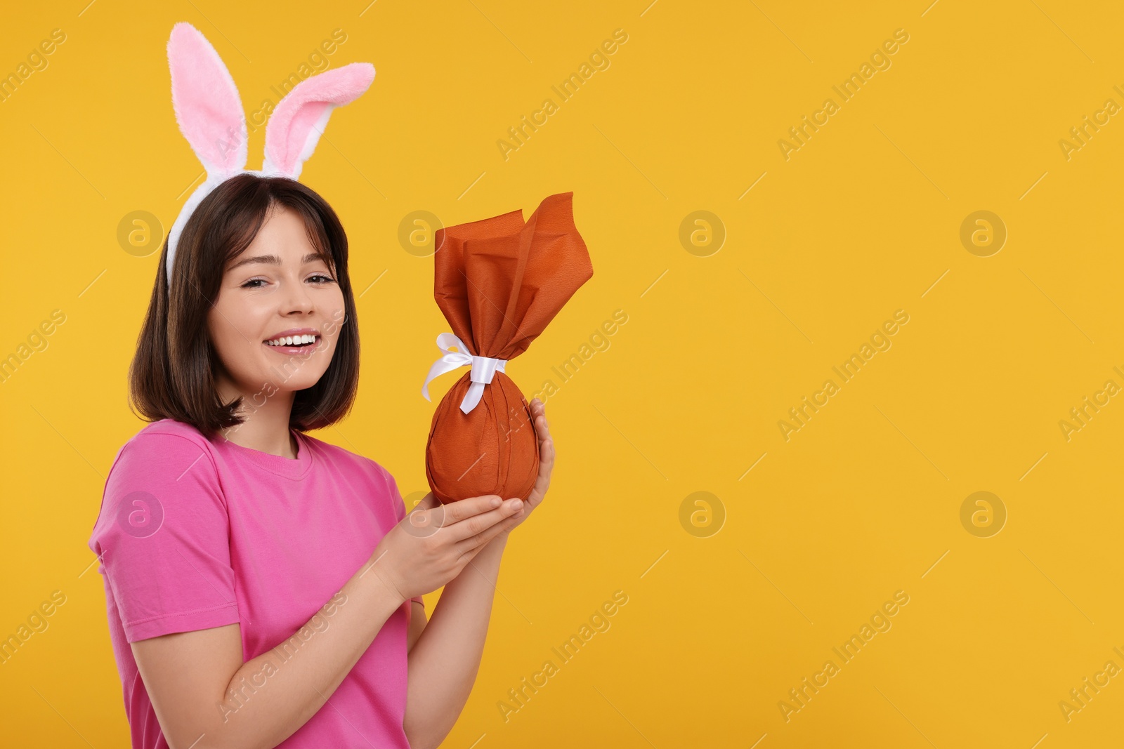 Photo of Easter celebration. Happy woman with bunny ears and wrapped egg on orange background, space for text