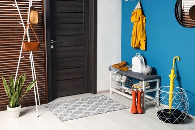 Photo of Hallway interior with stylish furniture, shoes and accessories near blue wall