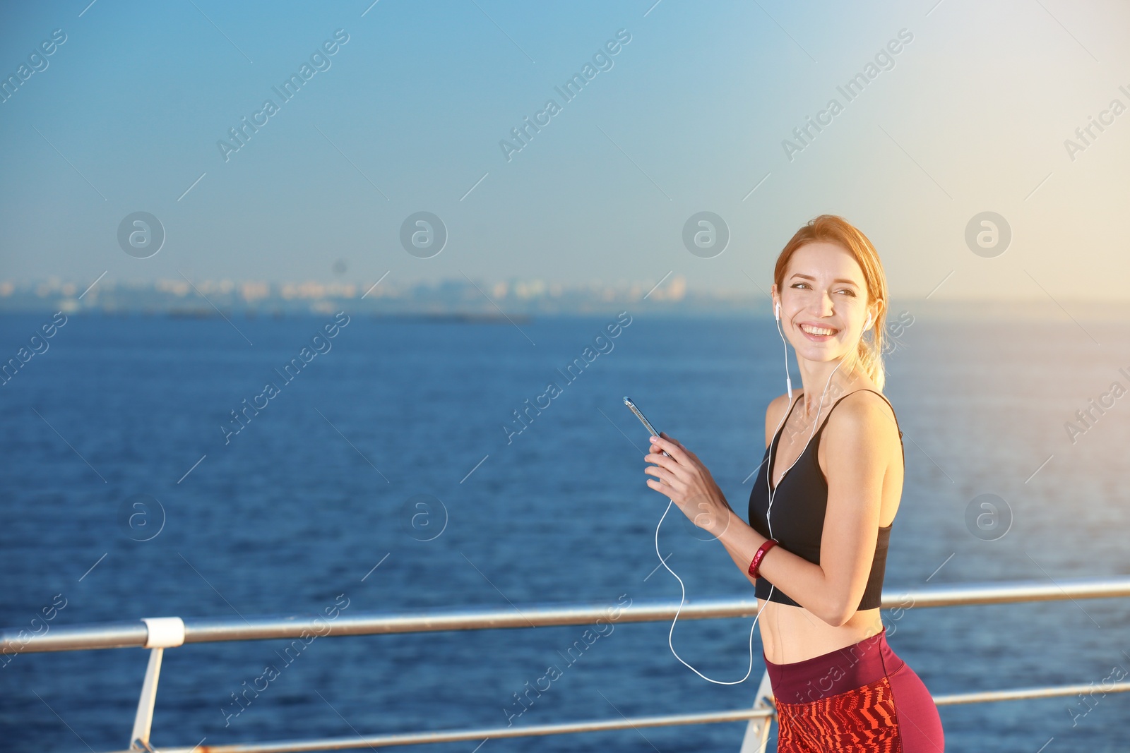 Photo of Young woman choosing music for fitness exercises on pier in morning