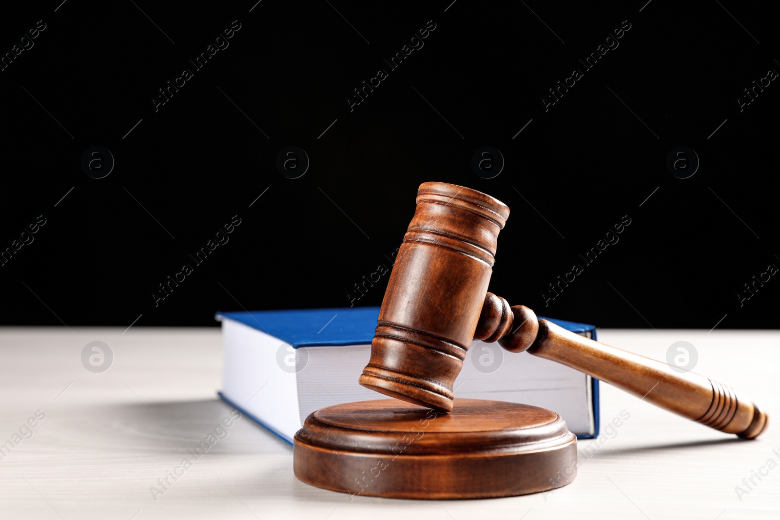 Photo of Judge's gavel and book on white table against black background. Criminal law concept