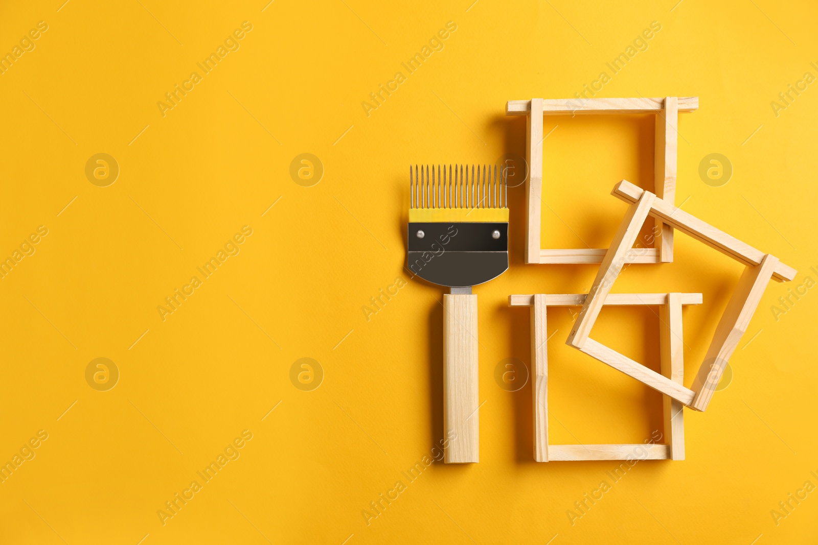 Photo of Uncapping fork and honeycomb frames on yellow background, flat lay with space for text. Beekeeping tools