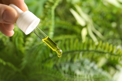 Photo of Woman holding pipette with oil on blurred background. Space for text