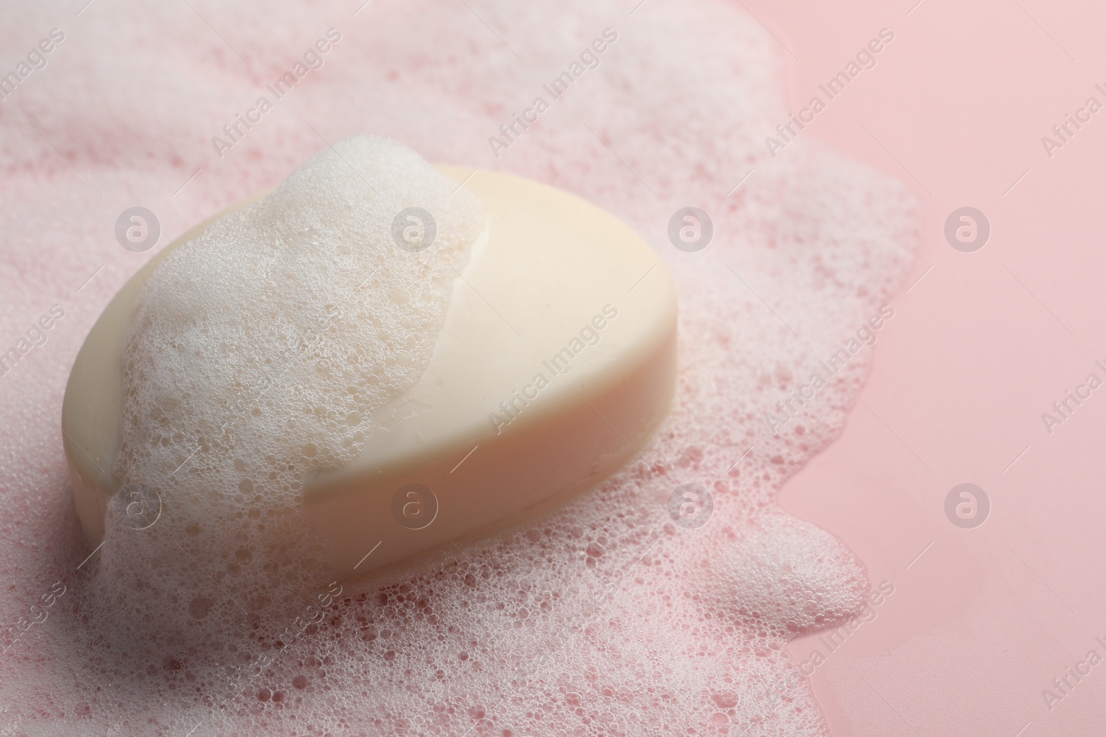 Photo of Soap with fluffy foam on pink background, closeup. Space for text