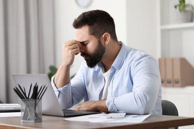 Photo of Man suffering from headache at workplace in office