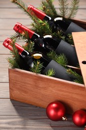 Photo of Wooden crate with bottles of wine, fir twigs and red Christmas balls on table