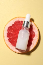 Photo of Bottle of cosmetic serum and grapefruit slice on wet yellow background, top view