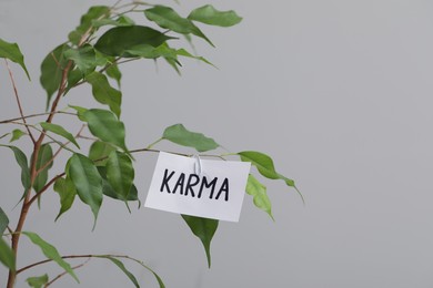Photo of Sheet of paper with word Karma on branch against grey background. Space for text