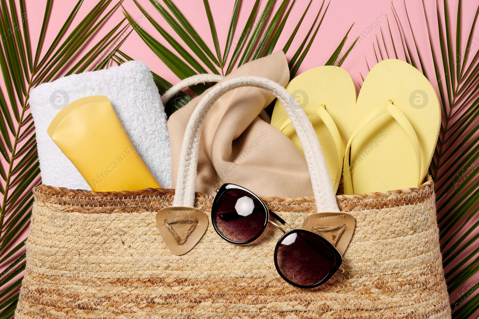 Photo of Flat lay composition with wicker bag, palm leaves and other beach accessories on pink background