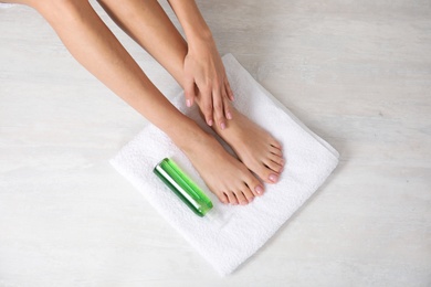 Photo of Woman with smooth feet, white towel and cosmetic on light background, top view. Spa treatment