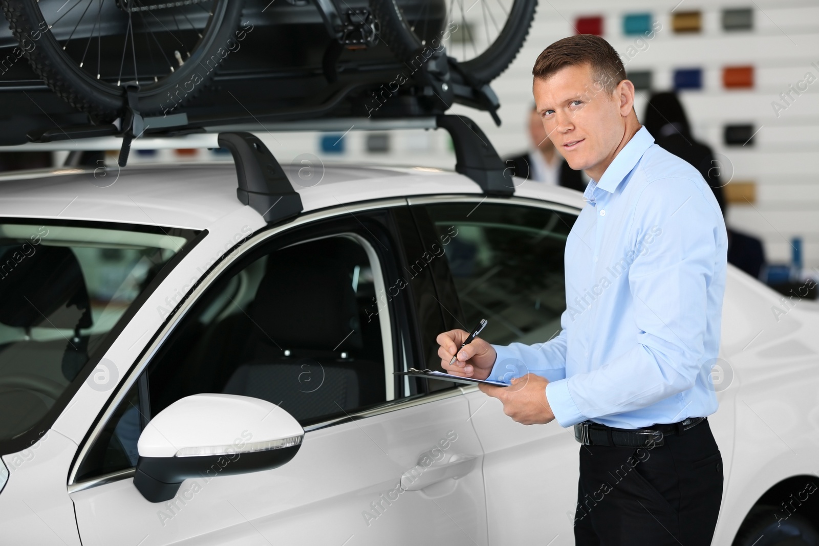 Photo of Young salesman with clipboard in car dealership