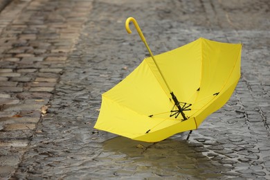 Photo of Open yellow umbrella on wet pavement. Space for text