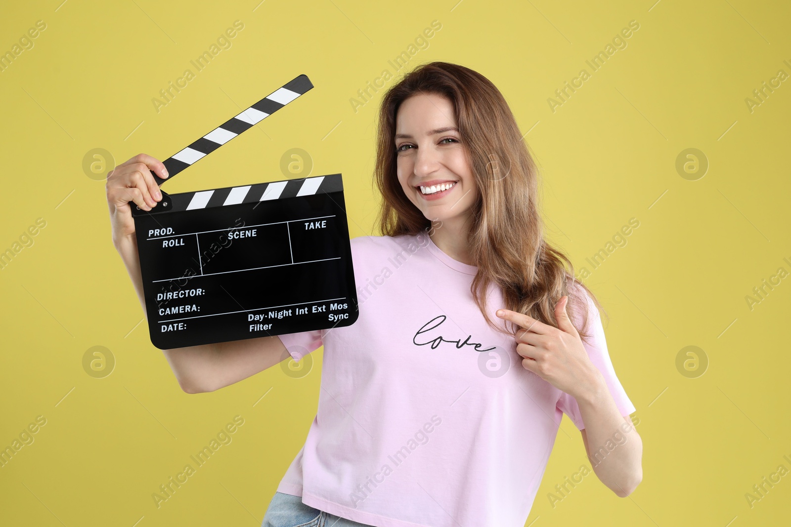 Photo of Making movie. Smiling woman pointing at clapperboard on yellow background