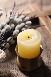 Burning church candle and willow branches on beige cloth, closeup