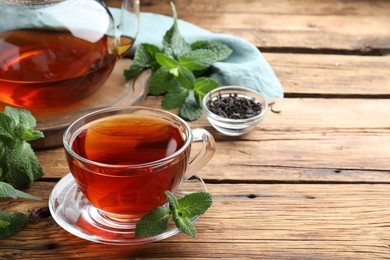 Cup of aromatic black tea with fresh mint on wooden table. Space for text