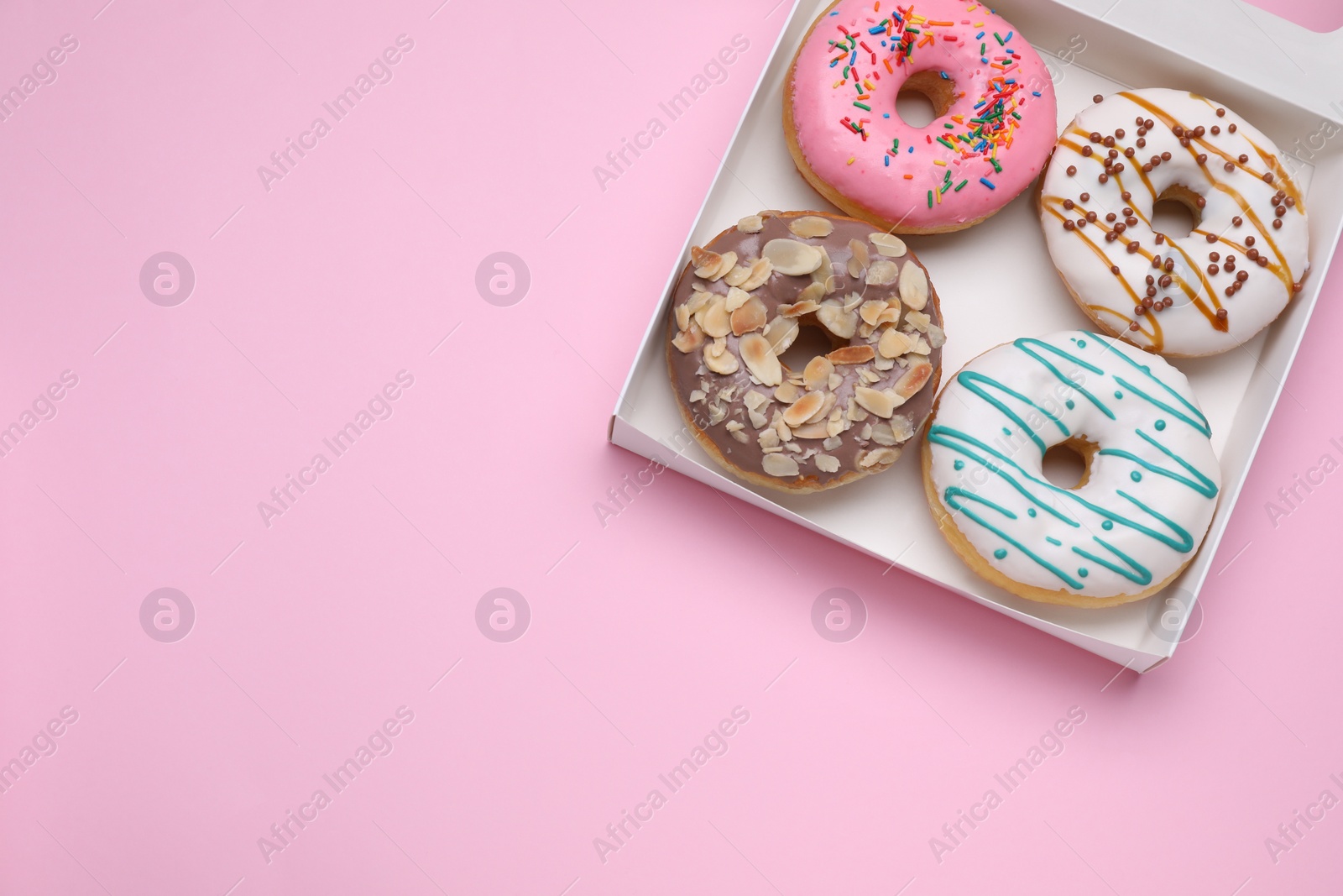 Photo of Box with different tasty glazed donuts on pink background, top view. Space for text