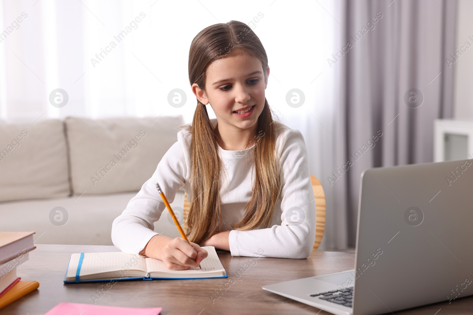 Photo of E-learning. Cute girl taking notes during online lesson at table indoors