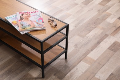 Photo of Wooden stand with magazines and glasses indoors. Modern furniture