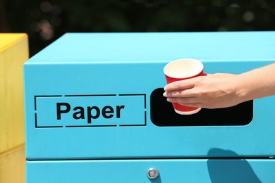 Woman throwing paper cup into sorting bin on city street, closeup. Recycling waste