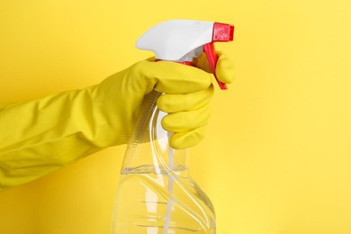 Woman holding plastic spray bottle on yellow background, closeup. Space for text