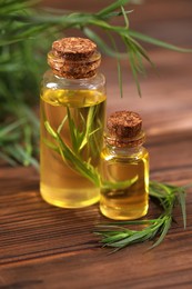 Bottles of essential oil and fresh tarragon leaves on wooden table