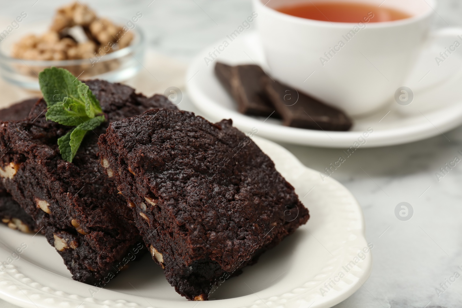 Photo of Delicious brownies with nuts and mint on white table, closeup. Space for text