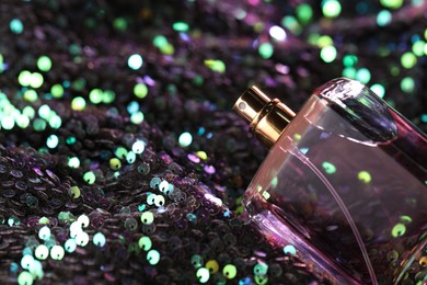 Photo of Luxury perfume in bottle on fabric with colorful sequins, closeup