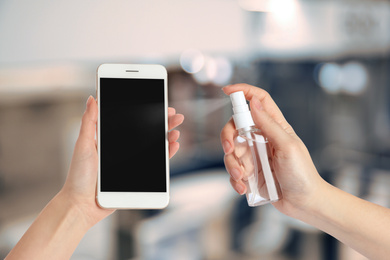Image of Woman sanitizing smartphone with antiseptic spray, closeup. Be safety during coronavirus outbreak 