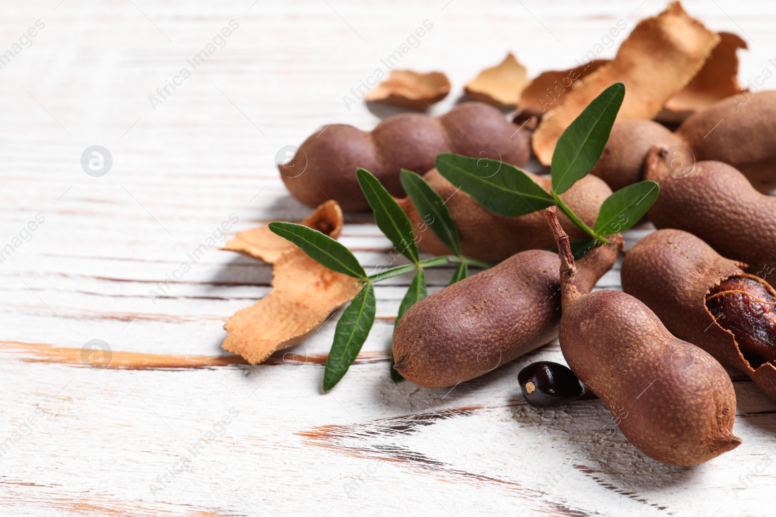 Photo of Delicious ripe tamarinds and leaves on white wooden table, closeup