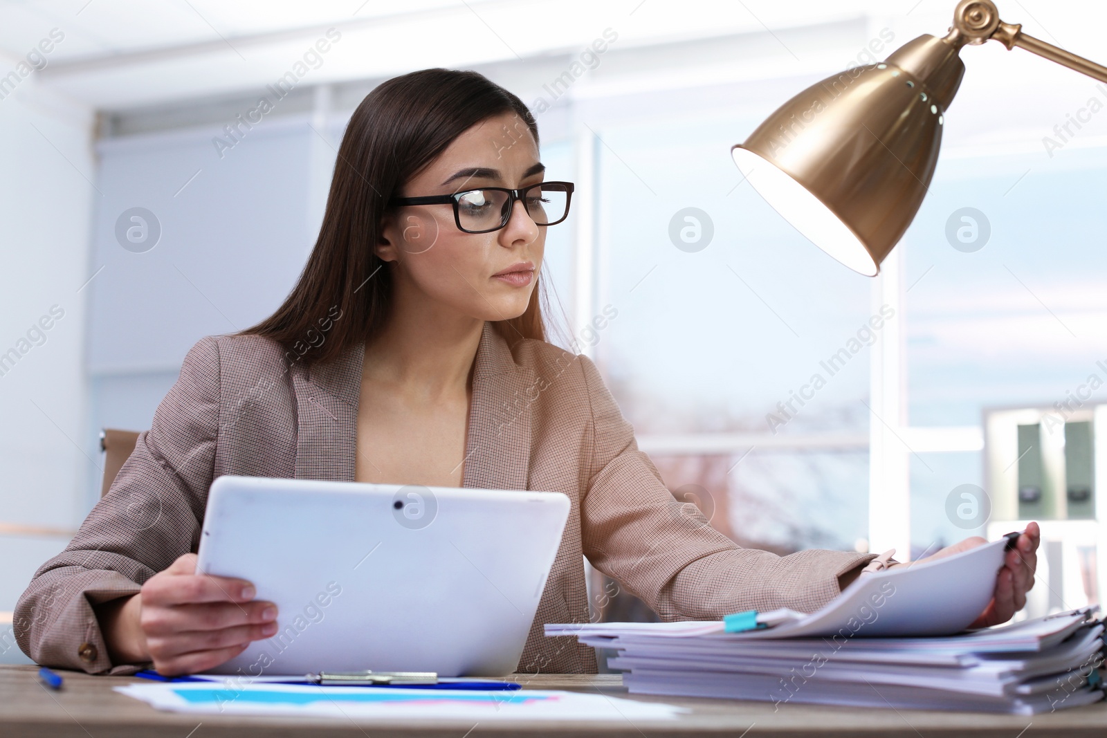 Photo of Businesswoman working with tablet and documents at table in office