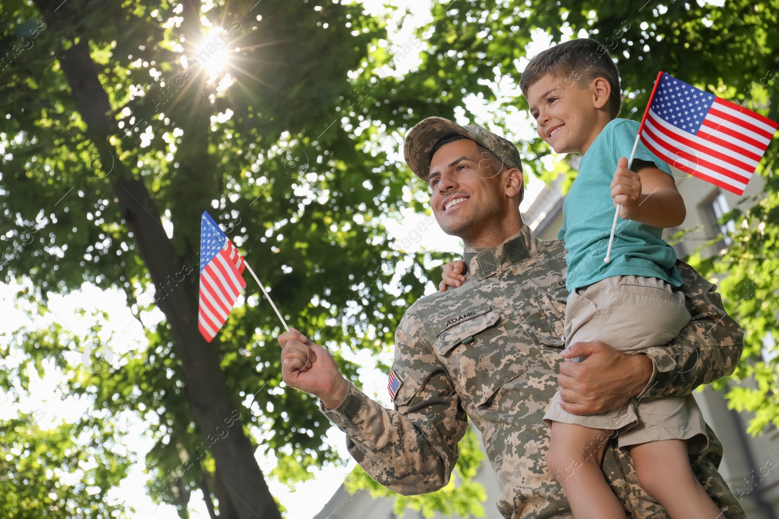 Photo of Soldier and his little son with American flags outdoors, low angle view. Veterans Day in USA